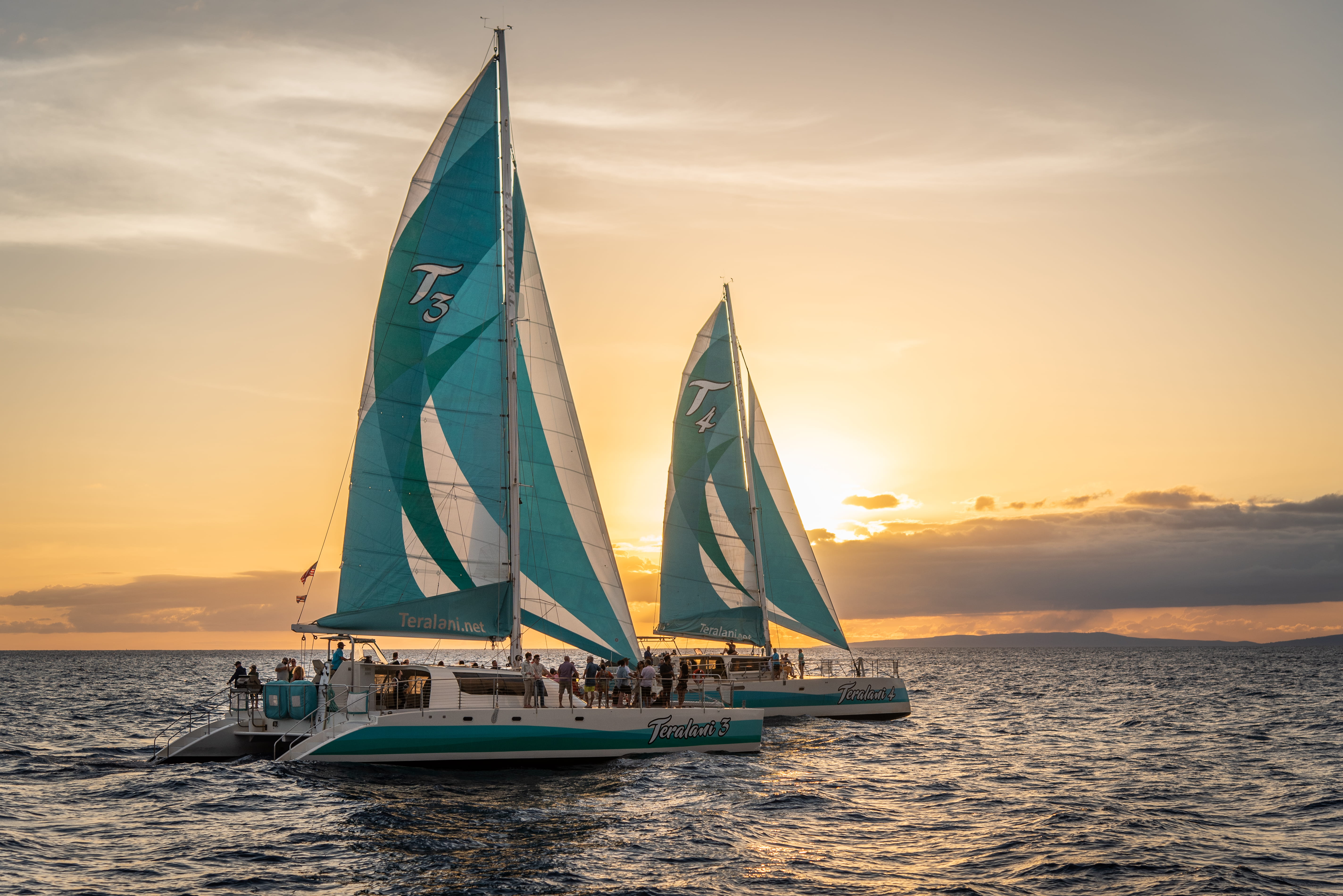 Two sailboats with turquoise sails at sunset on the ocean.